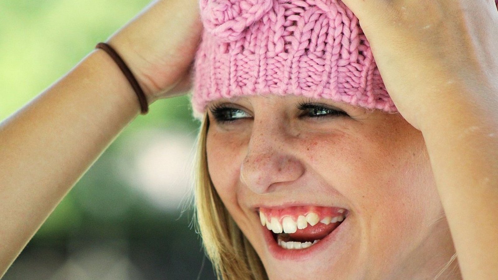 Ein jugendliches Mädchen hat eine rosa Strickmütze auf und greift sich mit den Händen an den Kopf. 