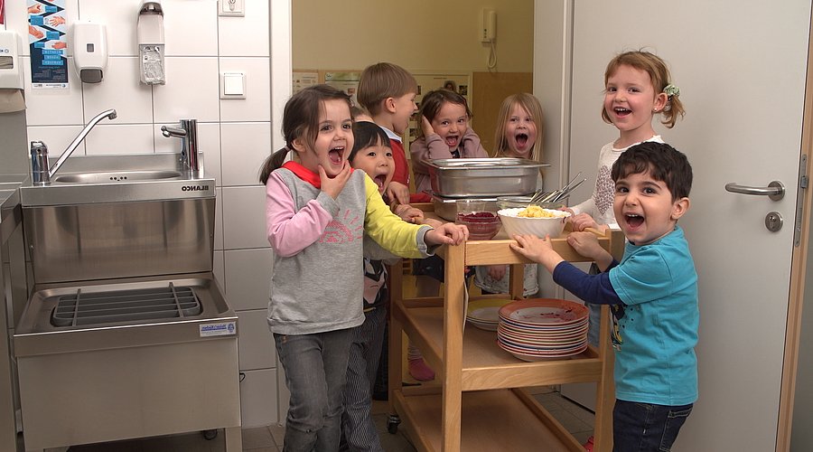 Kita-Kinder bringen schmutziges Geschirr nach dem Essen in die Küche.