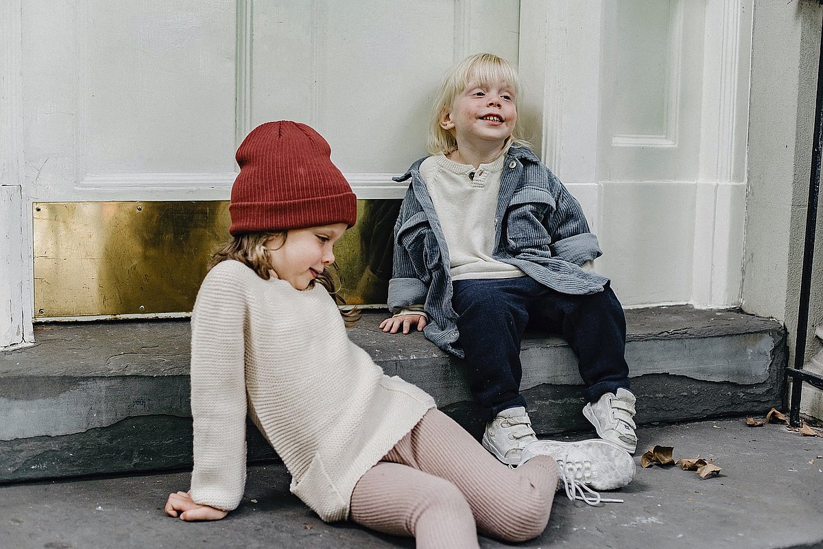 Zwei Mädchen im Schulkindalter sitzen vor einer Haustür auf dem Bordstein. 