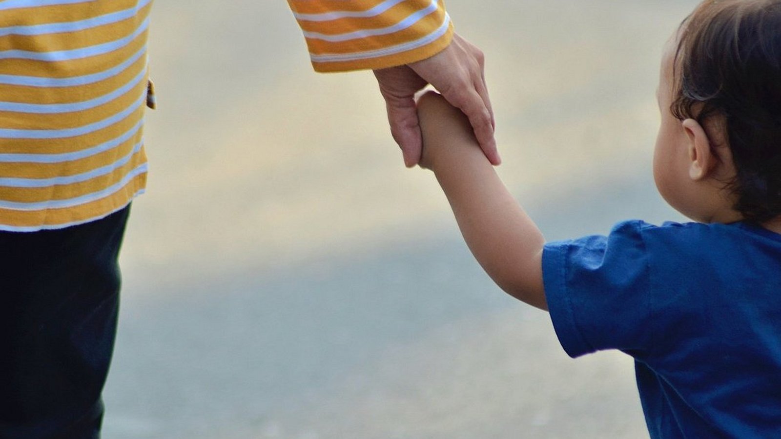 Ein Kleinkind geht an der Hand eines Erwachsenen.