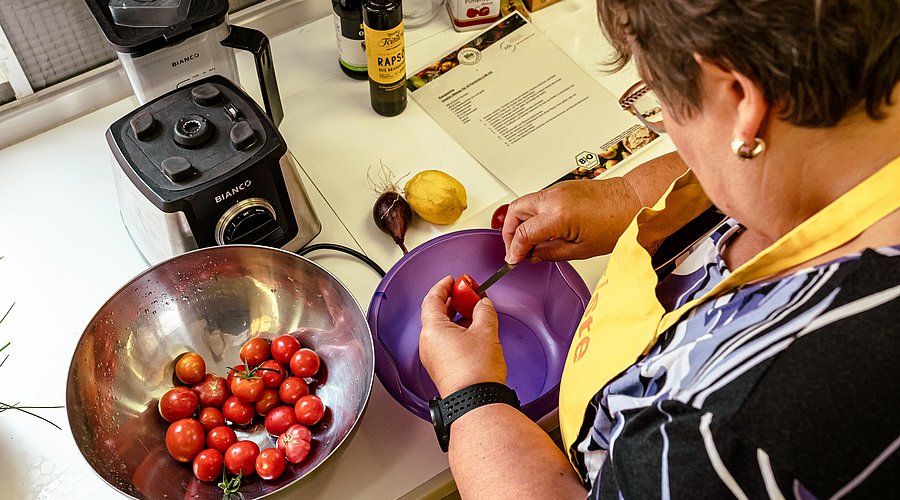 Eine Frau steht in einer Küche, mit Schürze, und putzt Obst.