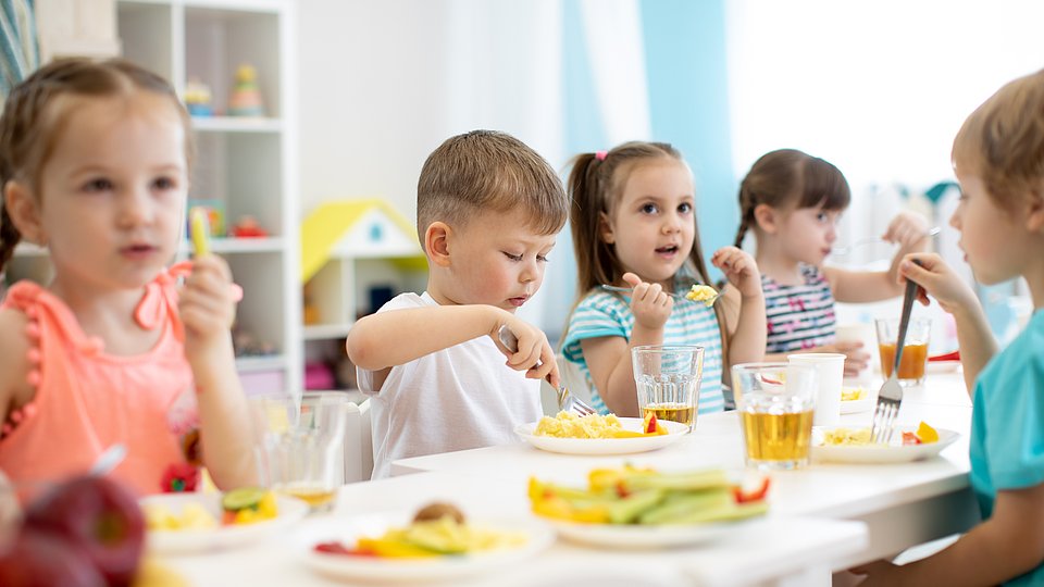 Kitakinder sitzen am Tisch und essen gemeinsam Mittag 