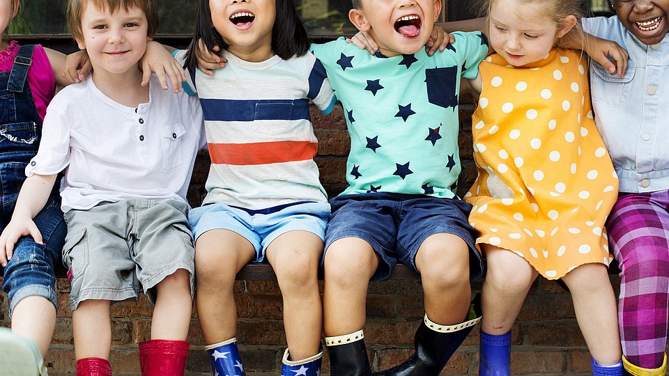 Kindergartenkinder sitzen nebeneinander auf einer Mauer und lachen