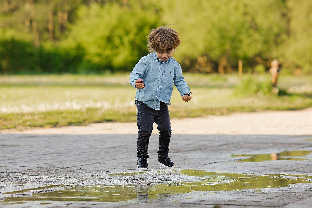 Ein Junge im Kindergartenalter springt in einer Pfütze auf und ab.