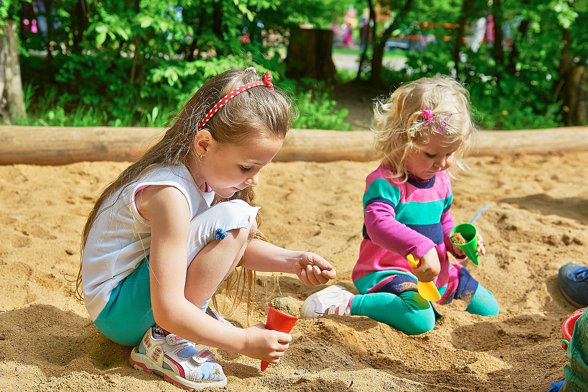 Ein Junge und ein Mädchem im Kita-Alter spielen in einem Sandkasten.