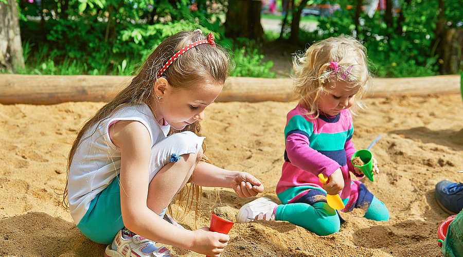 Ein Junge und ein Mädchem im Kita-Alter spielen in einem Sandkasten.