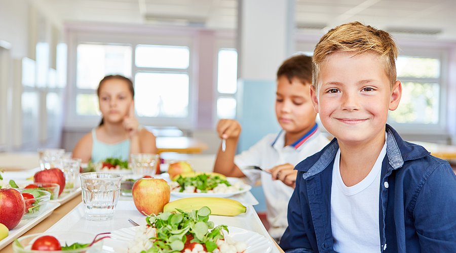 Schüler*innen sitzen in der Mensa an gefüllten Tellern.