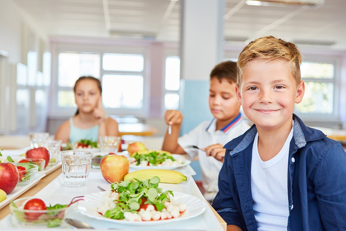 Schüler*innen sitzen in der Mensa an gefüllten Tellern.