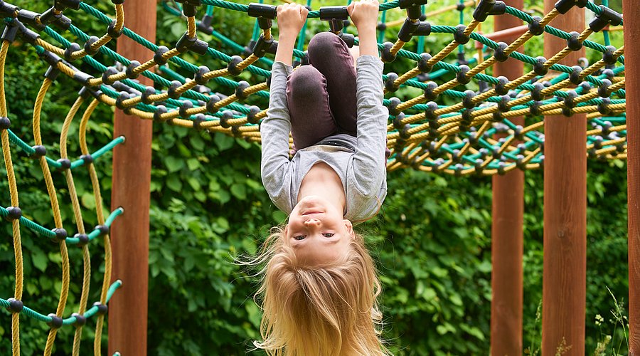 Ein Kita-Kind hängt kopfüber an einem Spielgerät.