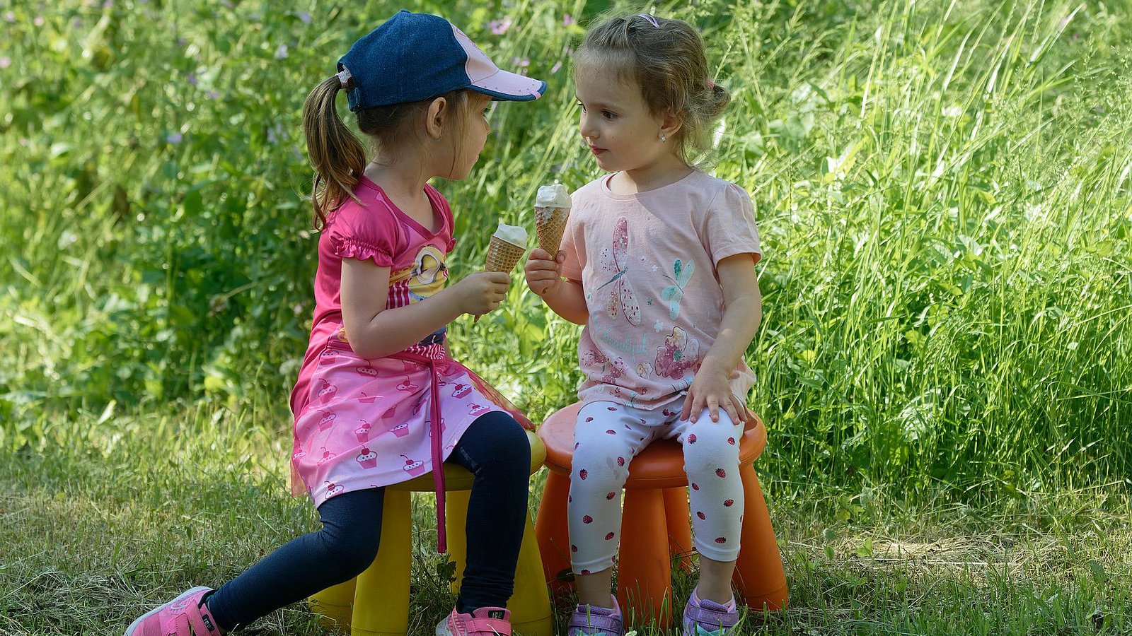 Zwei Kita-Mädchen sitzen im Garten und essen ein Eis. 