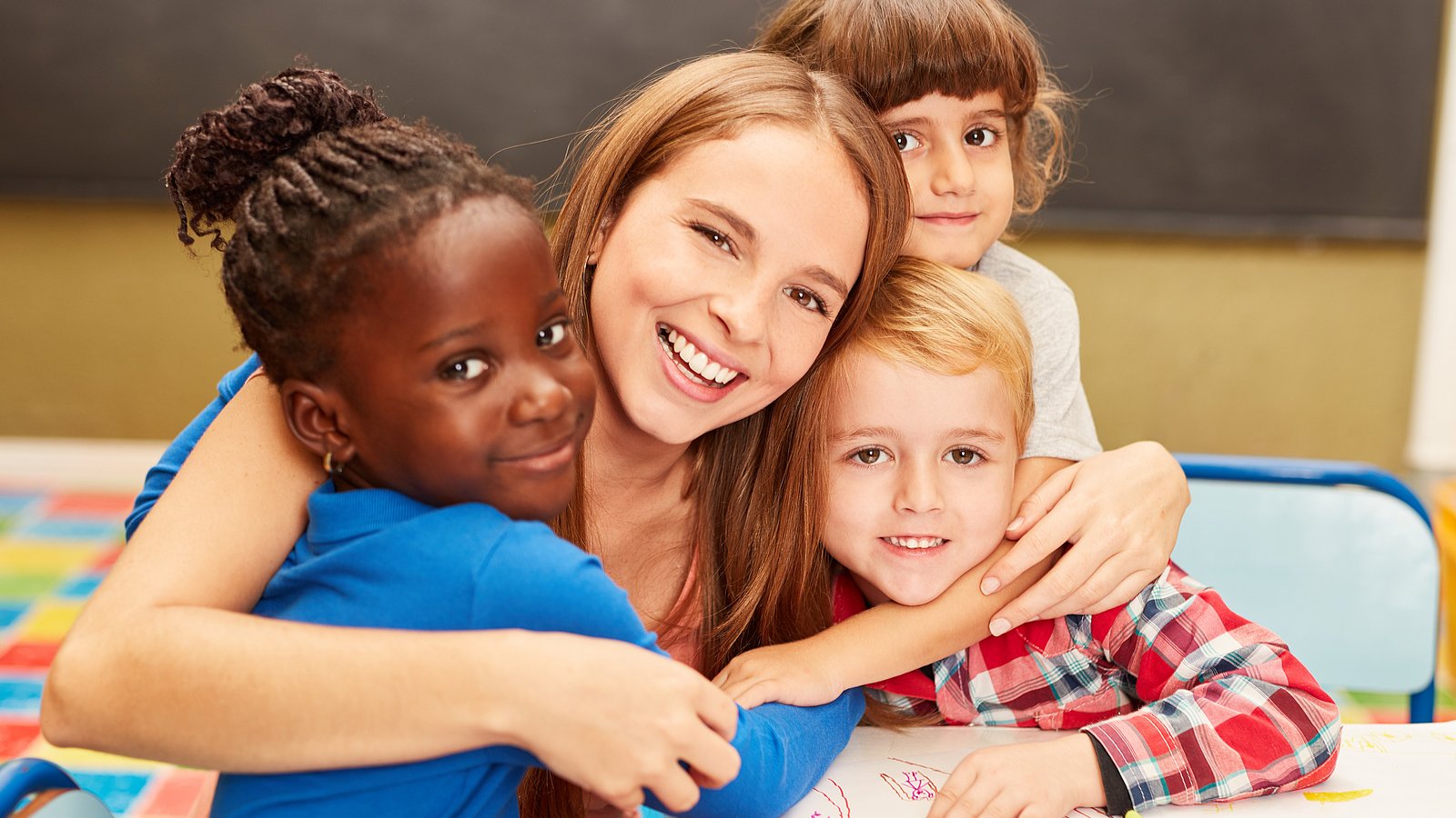 Eine pädagogische Fachkraft umarmt mehrere Kita-Kinder. 