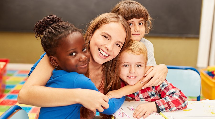 Eine pädagogische Fachkraft umarmt mehrere Kita-Kinder. 